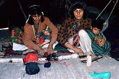 Women of the nomadic Kuchi people are expert carpet weavers and, while looking after their children, are at work in their black tent on the outskirts of Herat.